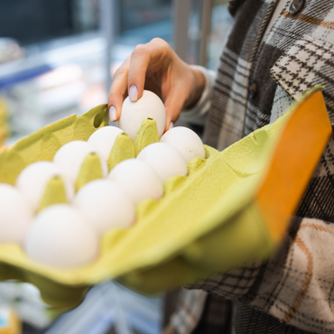 one hand holding a carton of eggs and the other hand picking up an egg